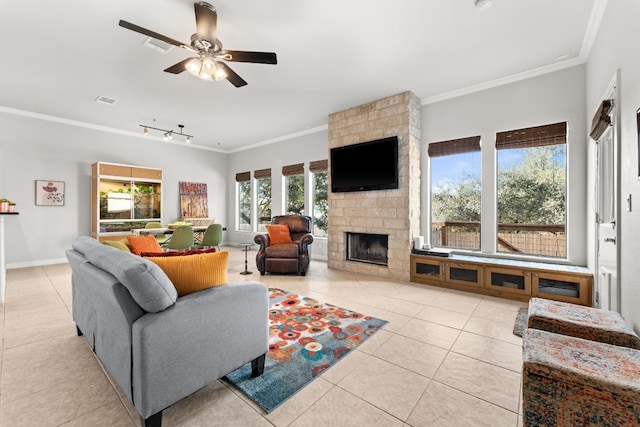 living room with crown molding, ceiling fan, a stone fireplace, and light tile patterned floors