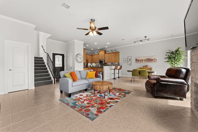 living room featuring light tile patterned floors, a ceiling fan, crown molding, visible vents, and stairs