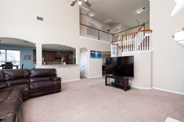 living room with ceiling fan with notable chandelier, a high ceiling, and light carpet