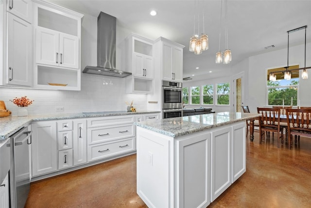 kitchen featuring a center island, white cabinets, wall chimney range hood, backsplash, and decorative light fixtures