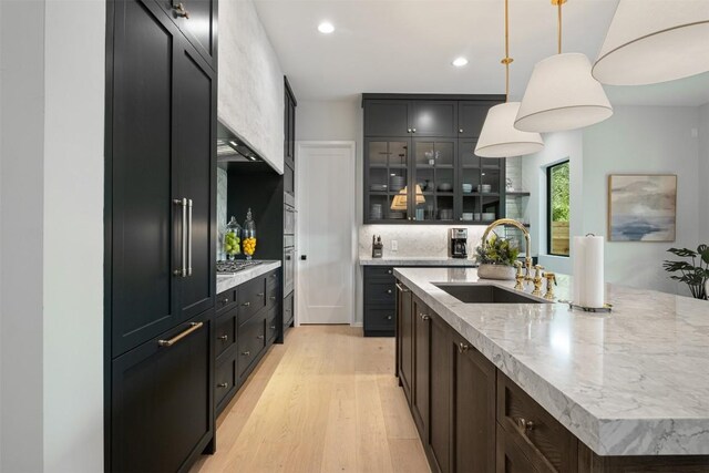 kitchen featuring a kitchen island with sink, sink, decorative backsplash, decorative light fixtures, and light hardwood / wood-style floors