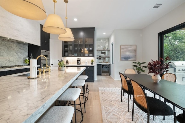 kitchen with light stone counters, stainless steel appliances, pendant lighting, light hardwood / wood-style floors, and wine cooler