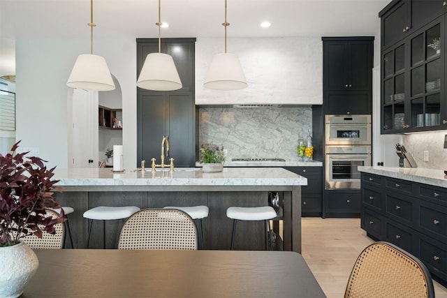 kitchen featuring a kitchen bar, appliances with stainless steel finishes, decorative light fixtures, and light hardwood / wood-style flooring