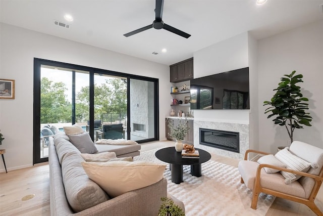 living room with a high end fireplace, light hardwood / wood-style flooring, and ceiling fan