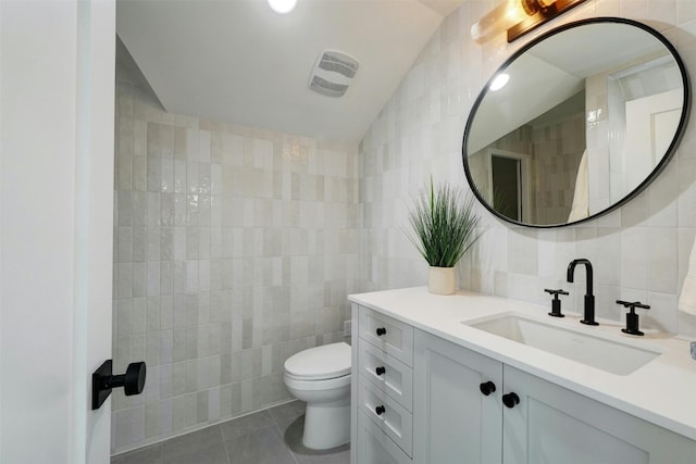 bathroom featuring tile patterned floors, vanity, vaulted ceiling, tile walls, and toilet