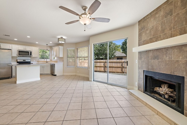 kitchen with stainless steel appliances, sink, a tile fireplace, light tile patterned floors, and white cabinets