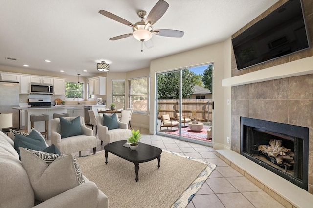 living area featuring light tile patterned floors, visible vents, a fireplace with raised hearth, and baseboards