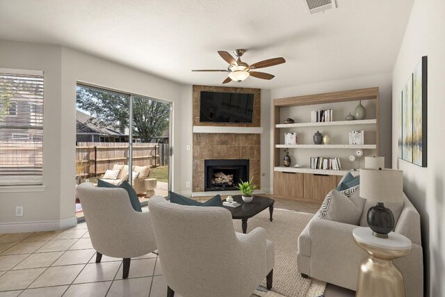 tiled living room with a tiled fireplace, built in features, and ceiling fan