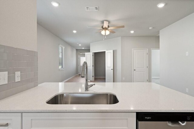 kitchen featuring sink, stainless steel dishwasher, tasteful backsplash, light stone counters, and white cabinetry