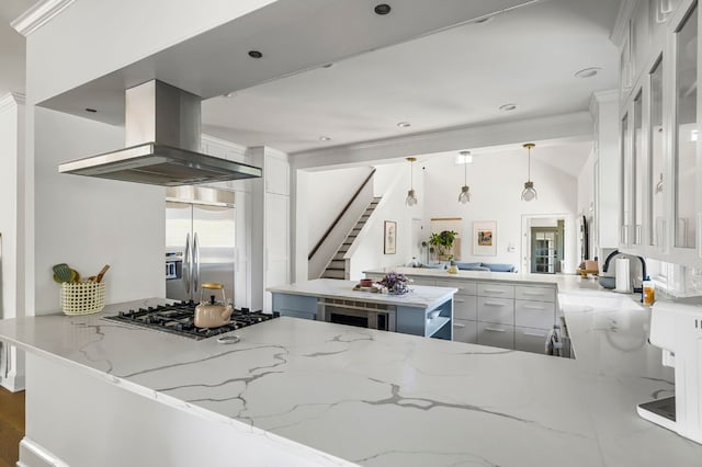 kitchen with island exhaust hood, light stone counters, a sink, a peninsula, and appliances with stainless steel finishes