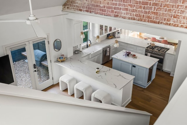 kitchen with dark wood finished floors, a sink, light stone countertops, appliances with stainless steel finishes, and brick wall