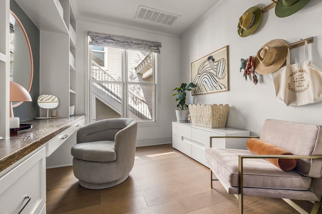 living area with light wood-style flooring, visible vents, built in desk, and crown molding