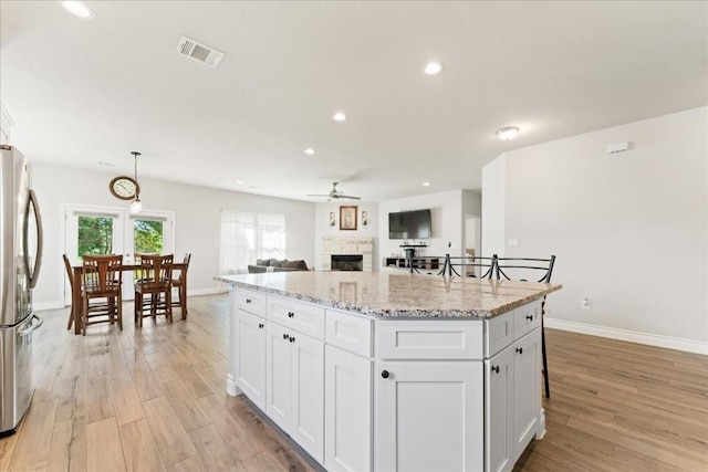 kitchen featuring white cabinetry, stainless steel fridge, a center island, light stone counters, and light hardwood / wood-style flooring