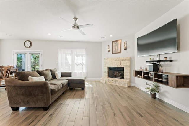 living area with a ceiling fan, a stone fireplace, light wood-style flooring, baseboards, and recessed lighting