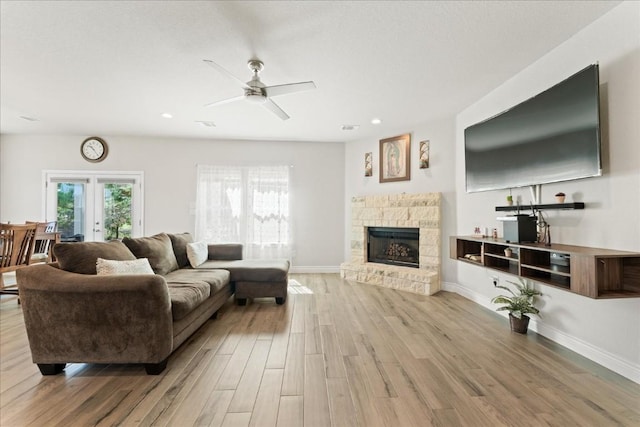 living room featuring french doors, ceiling fan, a fireplace, and light hardwood / wood-style flooring