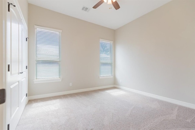 spare room with a healthy amount of sunlight, baseboards, visible vents, and light colored carpet