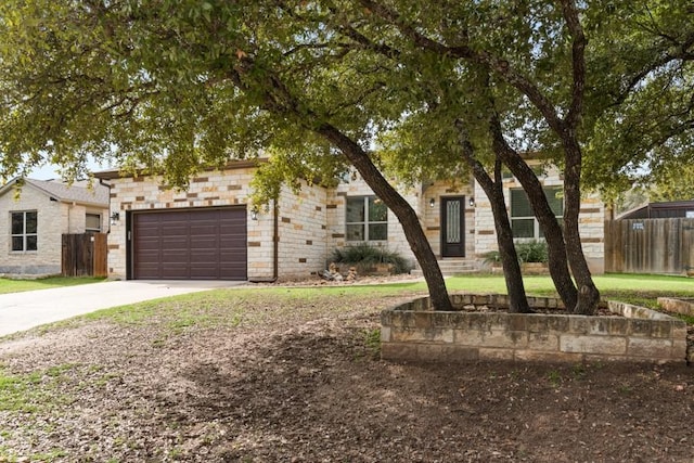 view of property hidden behind natural elements featuring stone siding, concrete driveway, fence, and an attached garage