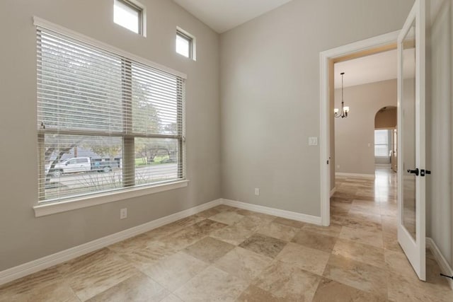 empty room featuring an inviting chandelier, baseboards, and arched walkways