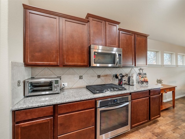 kitchen featuring light stone counters, stainless steel appliances, backsplash, and light hardwood / wood-style floors