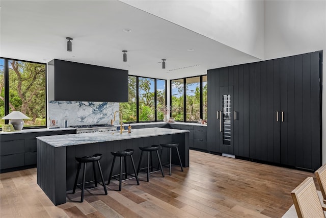 kitchen with light wood-type flooring, light stone counters, sink, a kitchen bar, and a spacious island