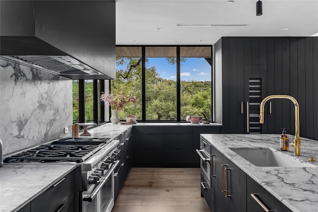 kitchen with a healthy amount of sunlight, high end stove, wall chimney range hood, and sink