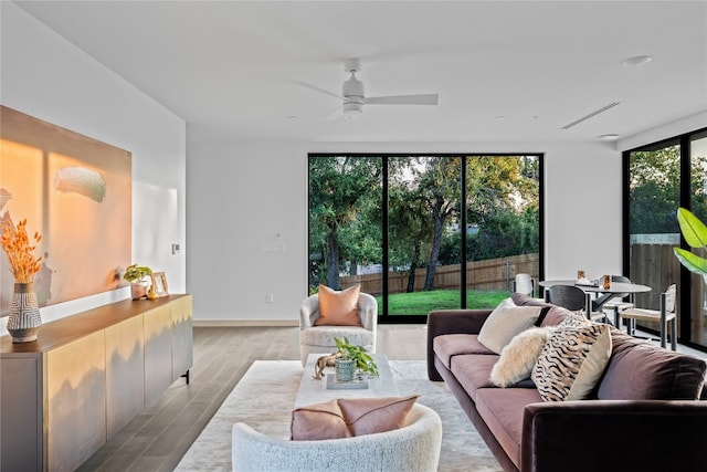 living room with a wall of windows, ceiling fan, and light hardwood / wood-style flooring