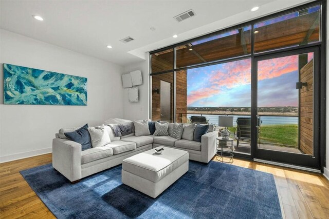 living room with expansive windows, a water view, and hardwood / wood-style floors