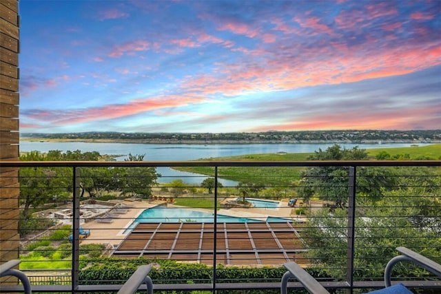 balcony at dusk featuring a water view