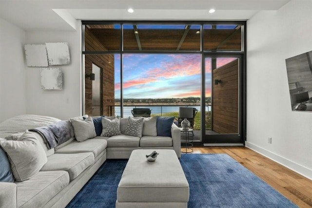 living room featuring a water view, baseboards, floor to ceiling windows, and wood finished floors