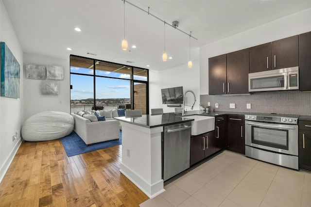 kitchen featuring pendant lighting, a wall of windows, stainless steel appliances, kitchen peninsula, and dark brown cabinets