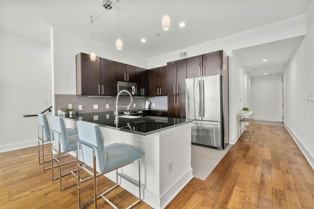 kitchen featuring dark brown cabinetry, tasteful backsplash, dark countertops, appliances with stainless steel finishes, and a peninsula