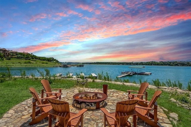 patio terrace at dusk with a water view, a dock, and a fire pit