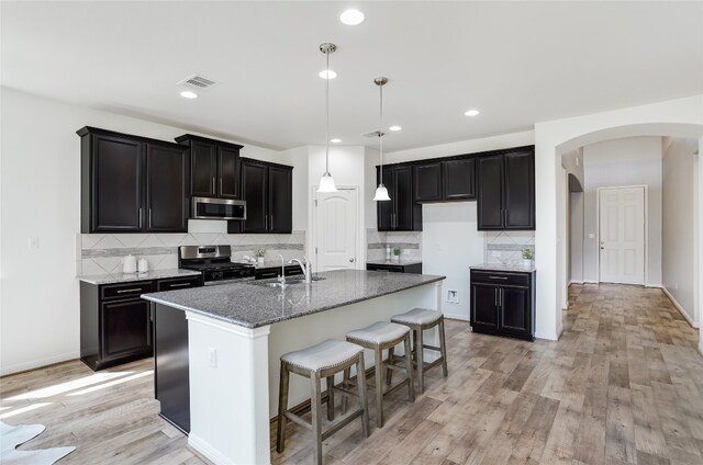 kitchen featuring stainless steel appliances, light hardwood / wood-style floors, an island with sink, and backsplash