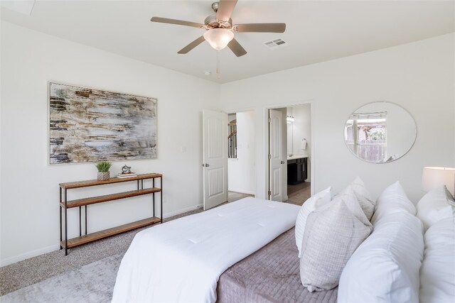 bedroom with ensuite bathroom, light colored carpet, and ceiling fan