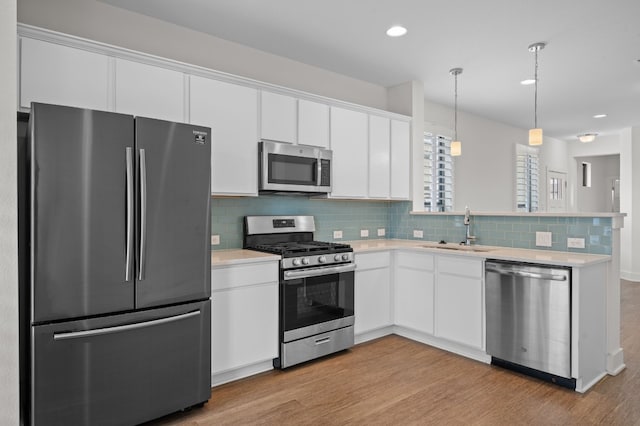 kitchen with pendant lighting, light hardwood / wood-style floors, sink, white cabinetry, and stainless steel appliances