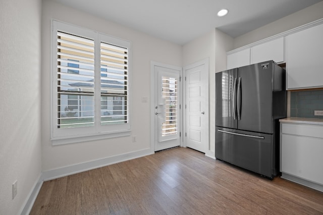 kitchen featuring white cabinets, stainless steel refrigerator, light wood-type flooring, and tasteful backsplash