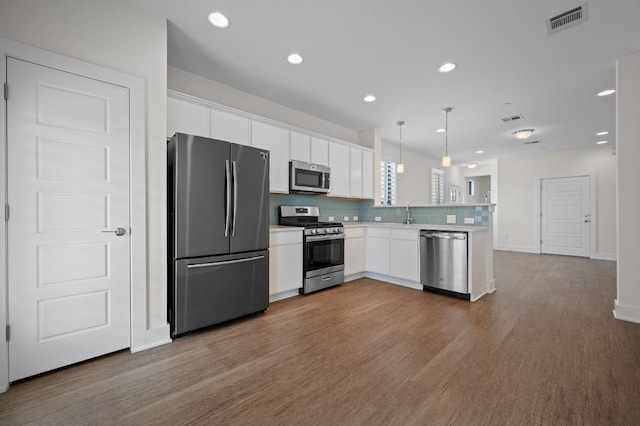 kitchen with white cabinets, kitchen peninsula, stainless steel appliances, wood-type flooring, and decorative light fixtures