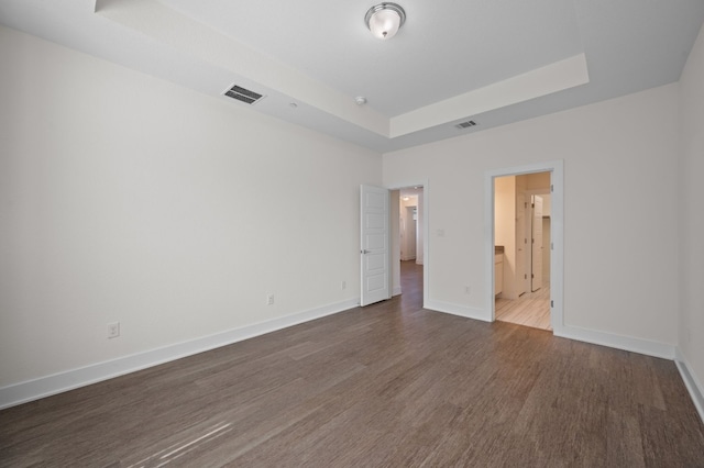 unfurnished bedroom with a raised ceiling, connected bathroom, and dark hardwood / wood-style flooring