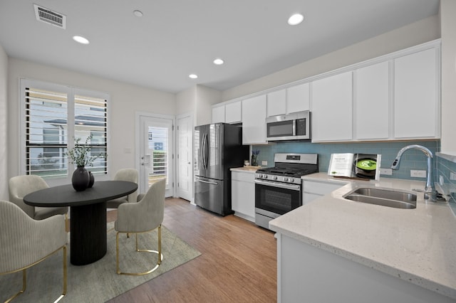 kitchen featuring light wood-type flooring, sink, white cabinetry, decorative backsplash, and appliances with stainless steel finishes