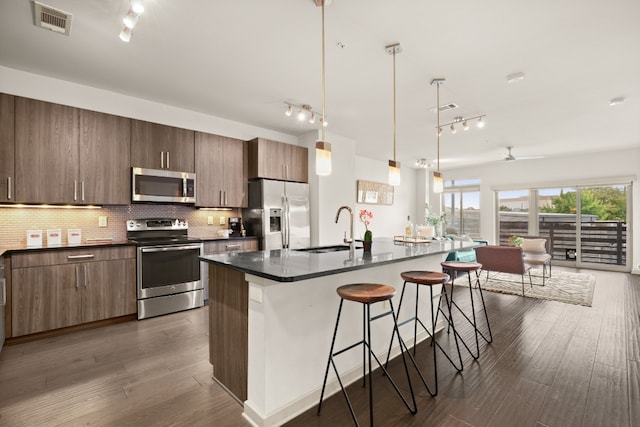 kitchen with appliances with stainless steel finishes, an island with sink, ceiling fan, dark hardwood / wood-style floors, and sink