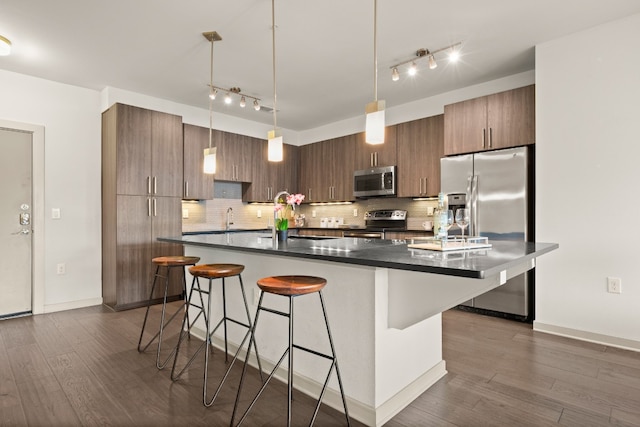 kitchen with backsplash, an island with sink, stainless steel appliances, and dark hardwood / wood-style floors