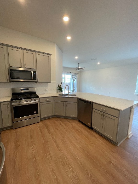 kitchen with ceiling fan, sink, kitchen peninsula, stainless steel appliances, and light hardwood / wood-style floors