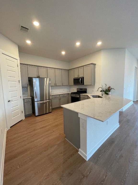 kitchen featuring gray cabinets, kitchen peninsula, stainless steel appliances, dark hardwood / wood-style flooring, and light stone countertops