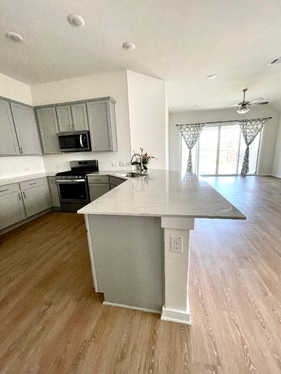 2421 Rosette Ln, Leander, TX 78641 - kitchen with stainless steel appliances, gray cabinetry, a peninsula, dark wood-style flooring, and light countertops