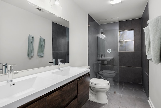 bathroom featuring vanity, toilet, a tile shower, and tile patterned flooring