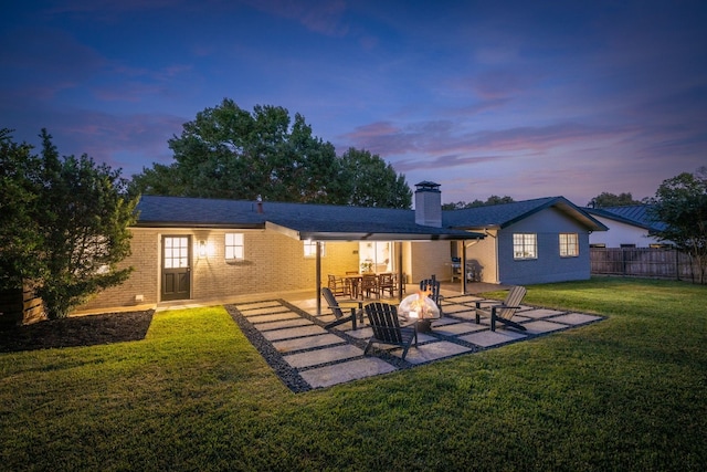 back house at dusk featuring a patio and a lawn