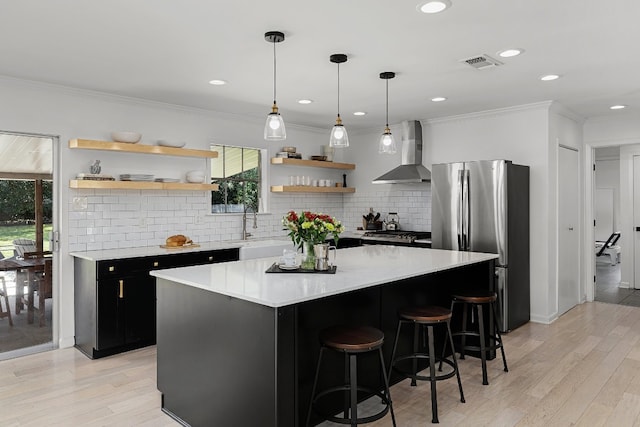 kitchen featuring wall chimney range hood, stainless steel appliances, plenty of natural light, and light wood-type flooring