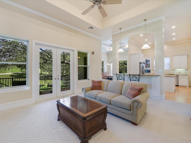 carpeted living room featuring a high ceiling, french doors, ceiling fan, ornamental molding, and a tray ceiling