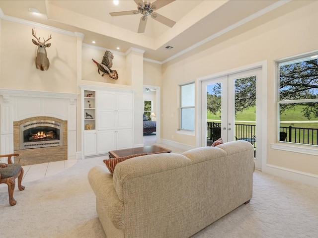 living room featuring a tile fireplace, a tray ceiling, plenty of natural light, and light colored carpet