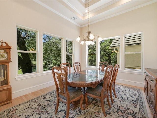 dining room featuring light wood-type flooring, a raised ceiling, a wealth of natural light, and ornamental molding